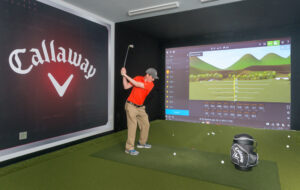 Commercial interior photo of a man hitting a golf ball in a golf simulator.